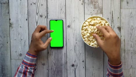 hombre de mano usando teléfono inteligente y comiendo palomitas de maíz