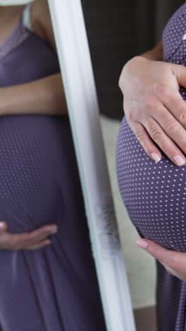 expecting white woman strokes tummy in front of the mirror. pregnant lady preparing for a childbirth. expectant mom in a pajama in her comfortable bedroom. vertical video