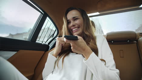 una mujer de negocios sonriente enviando un mensaje de voz en un teléfono inteligente en un coche moderno.