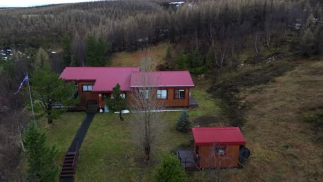 aerial drone reveals kirkjufellfoss forest landscape in iceland, panoramic view above woods, greenery and red houses, establishing shot