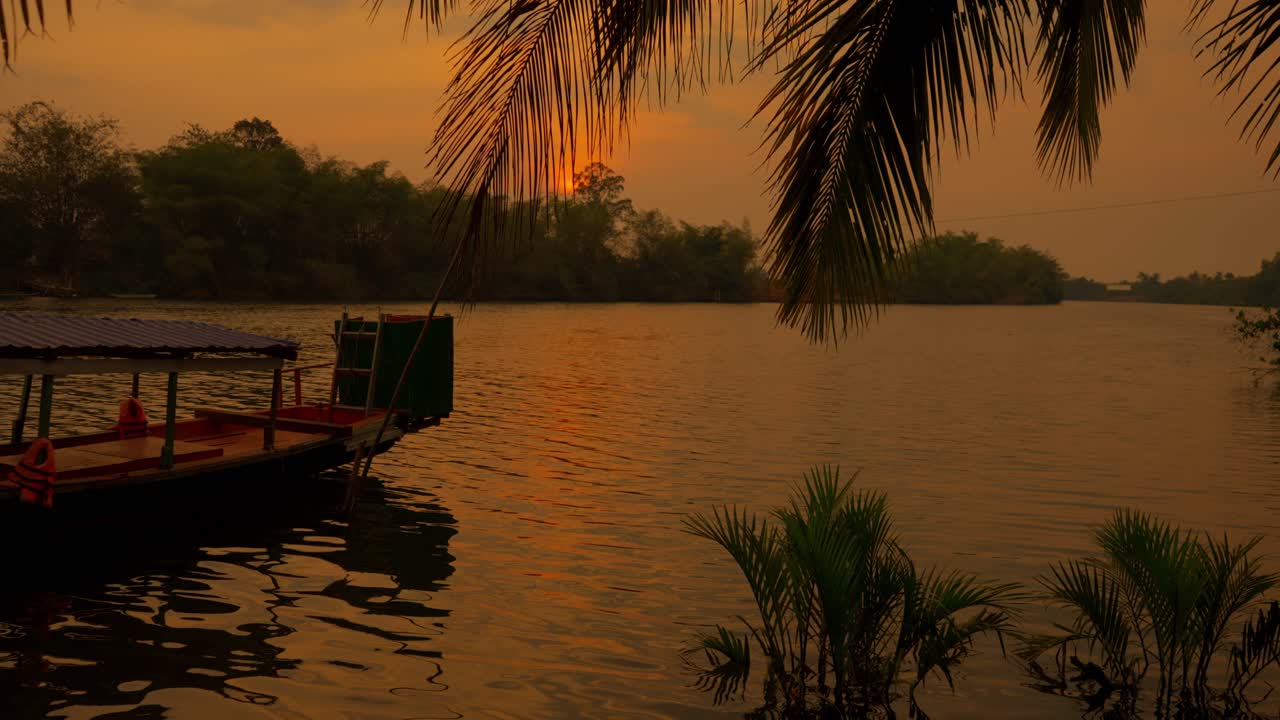 Calm tropical river at dusk with anchored boat and sunset reflecting in Cambodia