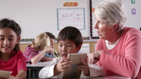 Teacher-helps-young-kids-using-tablet-computers-in-classroom