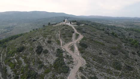 Fast-4K-drone-fly-by-over-2-ancient-rebuilt-windmills-on-top-of-the-hill-at-the-end-of-a-narrow-road-in-Alcublas,-Spain