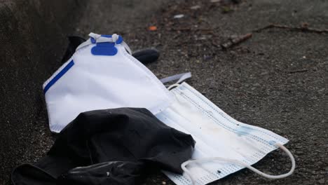 Dirty-discarded-used-corona-virus-masks-and-gloves-litter-on-street-blowing-in-wind-with-copy-space-dolly-left