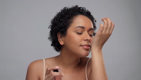 beauty,-perfumery-and-people-concept--portrait-of-happy-smiling-young-african-american-woman-with-bare-shoulders-applying-perfume-to-her-wrist-over-white-background