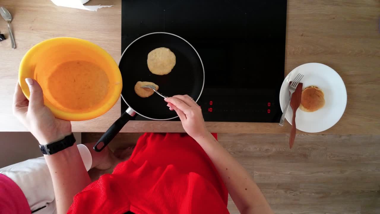 disparo superior de manos femeninas haciendo panqueques en una sartén negra caliente en la estufa eléctrica