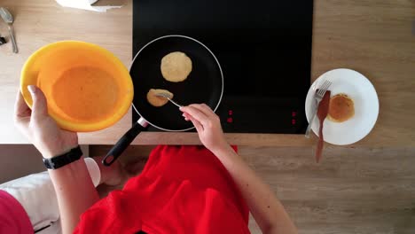 top down shot of female hands making pancakes on a hot black pan on electric stove