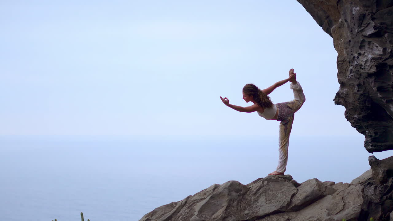 al atardecer, una joven hace yoga en una playa rocosa junto al océano azul, simbolizando un estilo de vida saludable, armonía y la conexión inherente entre los humanos y la naturaleza