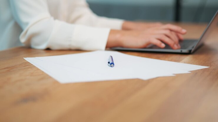 Blank white paper on wooden desk next to businesswoman working on laptop