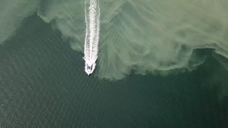 Draufsicht-Auf-Ein-Motorboot,-Das-Auf-Dem-Flachen-Blauen-Meer-Mit-Schlicksand-Auf-Dem-Meeresboden-Segelt---Antenne