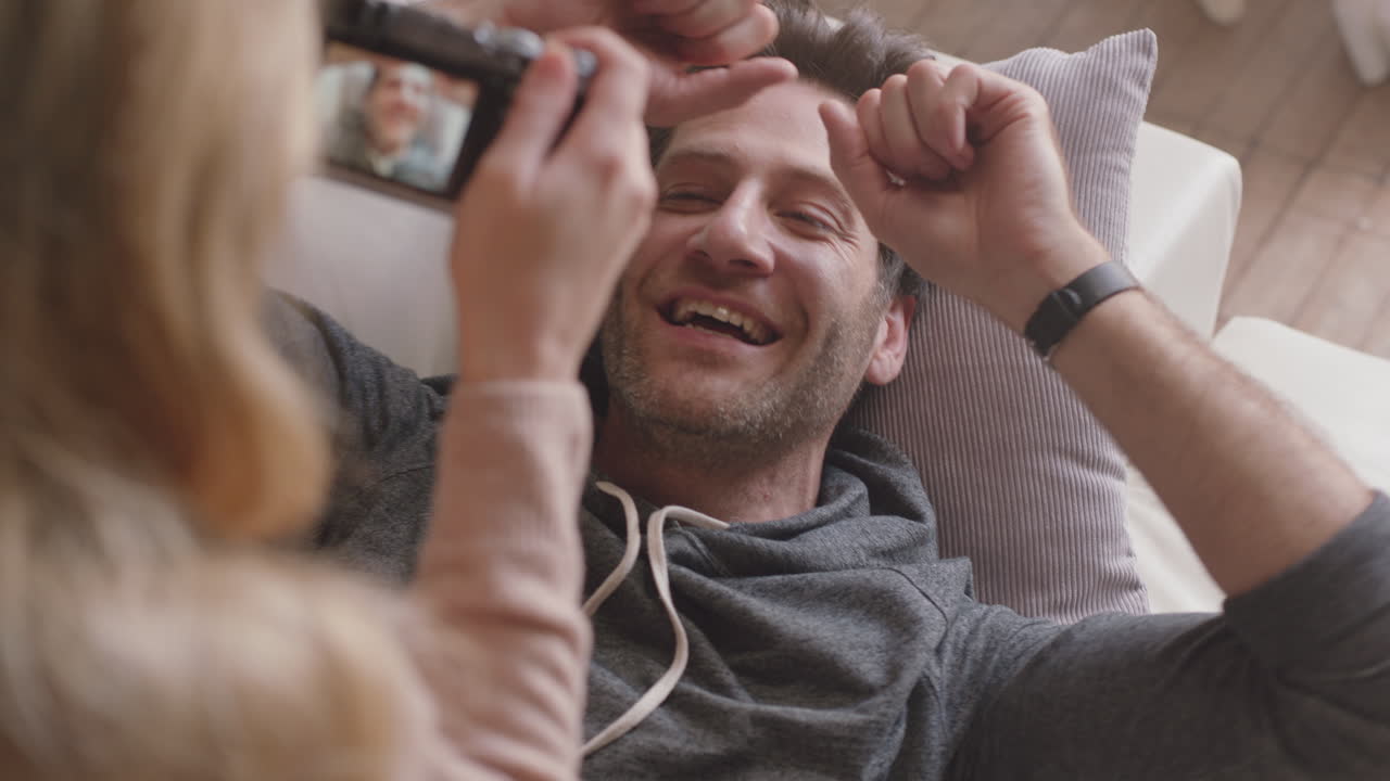 giovane coppia felice che scatta foto insieme usando la fotocamera divertendosi a casa sul divano godendosi giocosamente di una relazione romantica fotografandosi a vicenda facendo facce