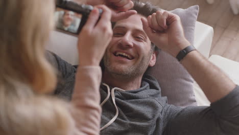 Feliz-Pareja-Joven-Tomando-Fotos-Juntos-Usando-Una-Cámara-Divirtiéndose-En-Casa-En-El-Sofá-Disfrutando-Juguetonamente-De-Una-Relación-Romántica-Fotografiándose-Unos-A-Otros-Haciendo-Muecas