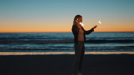 Frau-Spielt-Mit-Wunderkerzen-Am-Strand-Bei-Sonnenuntergang-Und-Genießt-Die-Silvesterfeier.-Mädchen-Feiert-Den-Unabhängigkeitstag-Und-Schwenkt-Wunderkerzen-Feuerwerk-Am-Meer