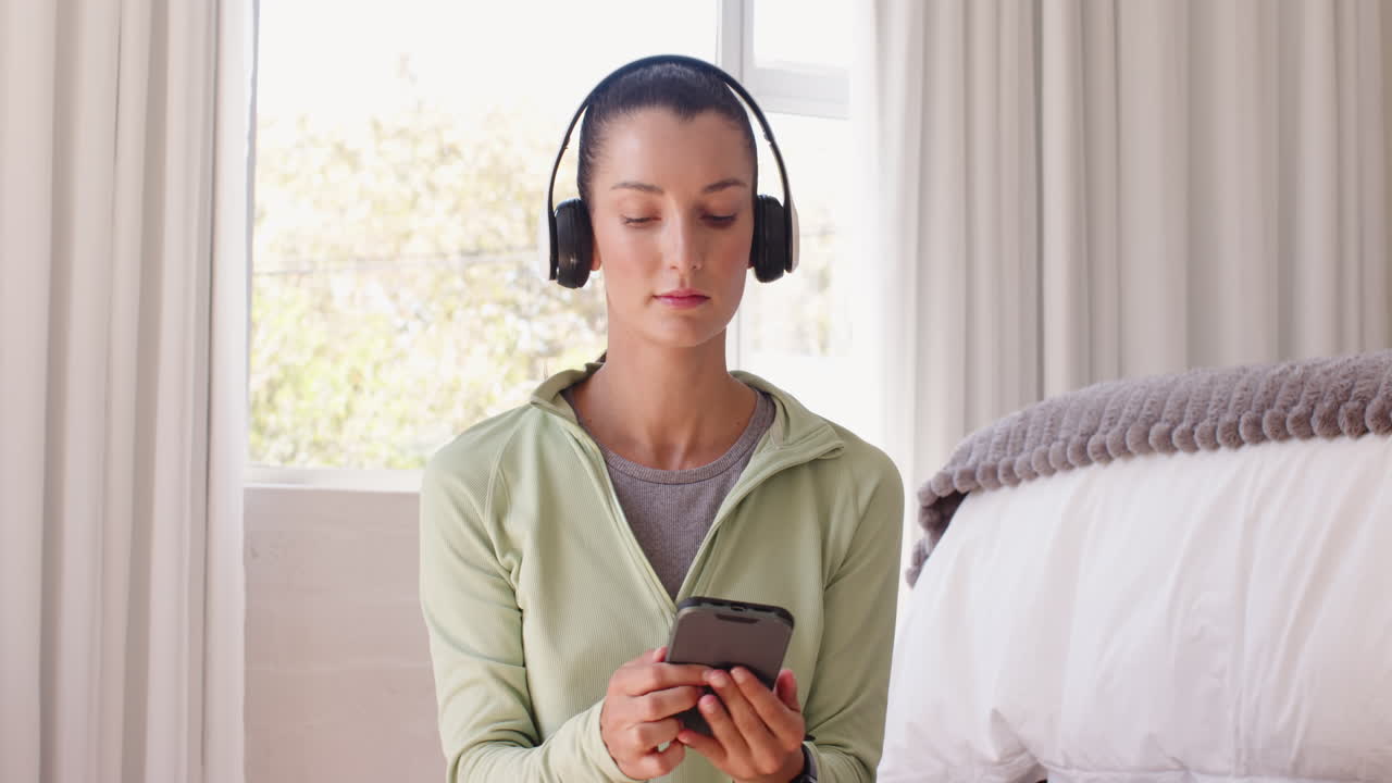 Wearing headphones, woman using smartphone listening to music at home