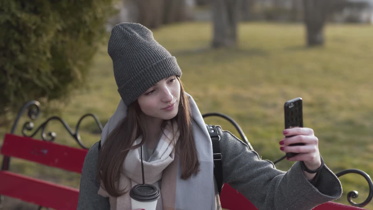 mujer caucásica tomando un selfie en un banco del parque
