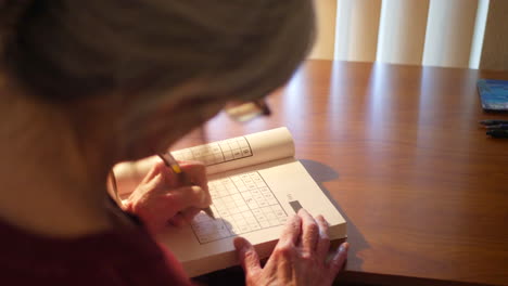 middle aged caucasian woman with aging hands solving a number puzzle book for mind acuity to stay mentally adept and sharp