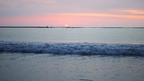 sun peaks over the horizon as small waves come onto the beach in slow-motion