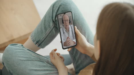 female medical assistant wears white coat headset video calling distant patient on smartphone. doctor talking to client using virtual chat telephone app. telemedicine remote healthcare services