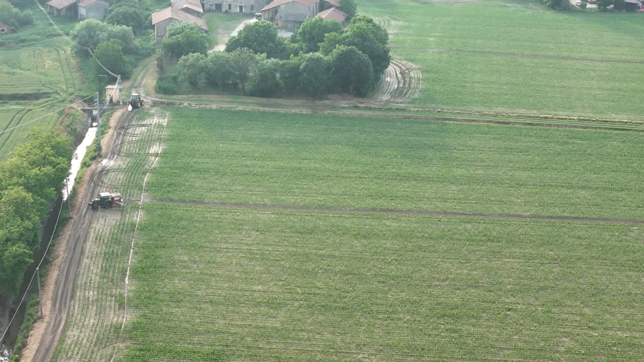 드론이 녹색 들판에 제초제를 뿌리는 트랙터 위로 올라가 현대 농업에서 작물 처리의 규모, 정확성, 복잡성을 보여주고, 식품 안전이 균형을 이루도록 해요.