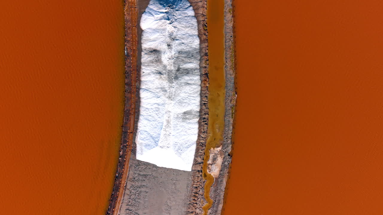 A salt pile dike in pink water. Abstract aerial pattern of a white salt ridge and grey path dividing deep orange-pink water