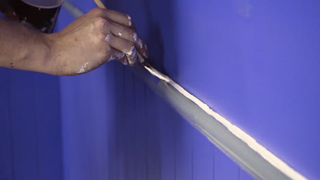 medium shot of a hand painting a white strip on a blue wall