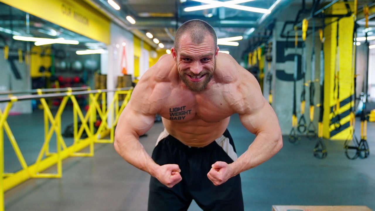 Bodybuilder muscoloso che flette bicipiti e petto in una palestra