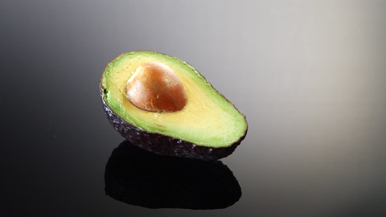 Un avocado verde maturo tagliato a metà con il nocciolo isolato su uno sfondo in bianco e nero