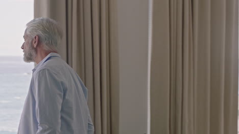 mature man in hotel room on vacation looking out window contemplating lifestyle planning ahead enjoying relaxing retirement