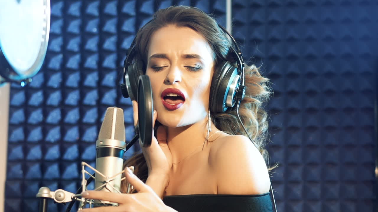 Vinnitsa, Ukraine - May 2019: Audio recording studio. Woman with headphones and studio microphone singing. Slow motion