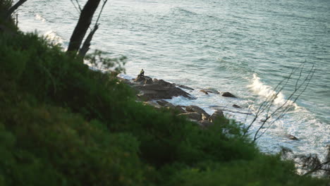 Vista-De-Cabecera-Del-Comerciante-Sentado-En-La-Roca-En-La-Playa-Con-Olas-Rompiendo,-4k