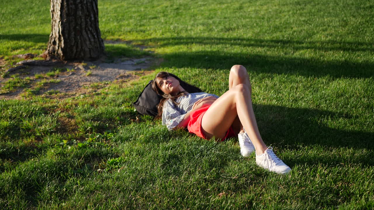 Beautiful young hispanic college student resting on a grassy field between classes on campus