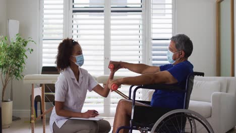 fisioterapeuta de raza mixta que usa una máscara ayudando a los ancianos a hacer ejercicio usando pesas