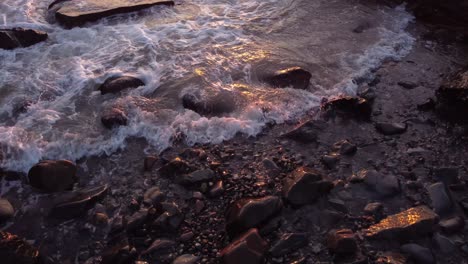 aerial of rocky beach with ocean waves crash in to coastline during sunset golden hours light
