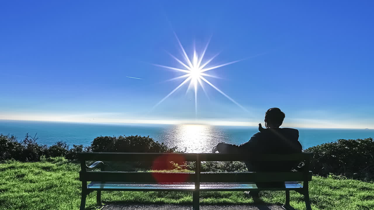 공원 벤치에 앉아 태양이 물에 반사되는 바다를 바라보는 청년 - 사이딩 시간 경과