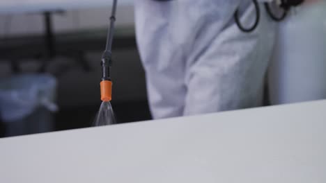 midsection of cleaner wearing protective overalls disinfecting office and furniture