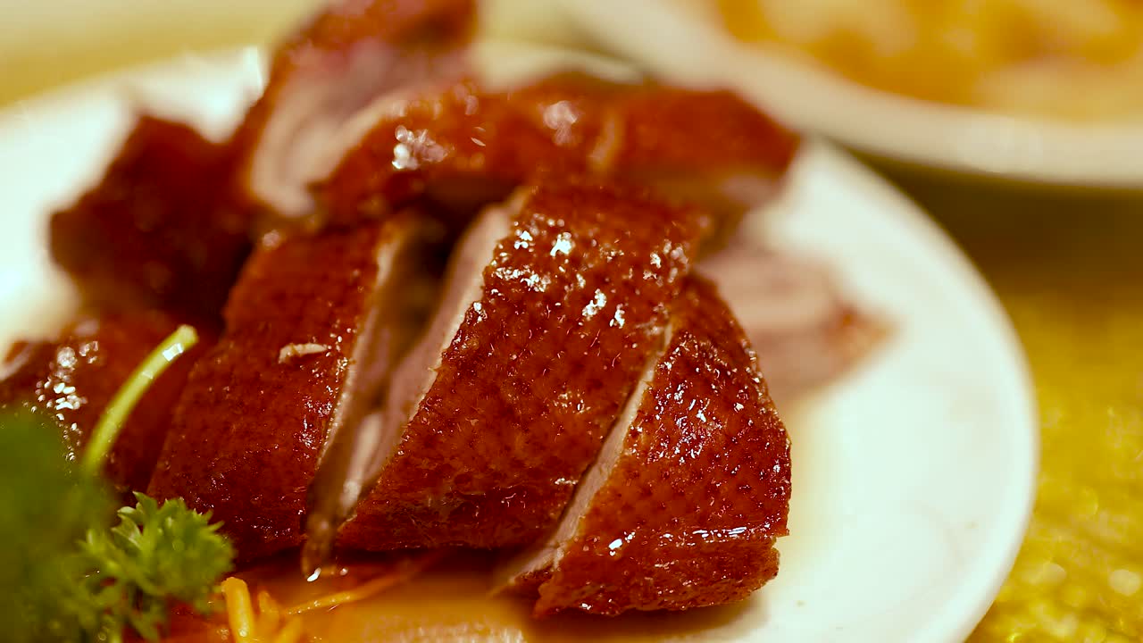 Close-up of sliced roast duck on a white plate, highlighting its glossy texture and rich color under warm lighting