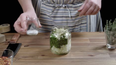 chef adding spices to jar to make chimichurri, bay leaf, salt, dried chili and oregano