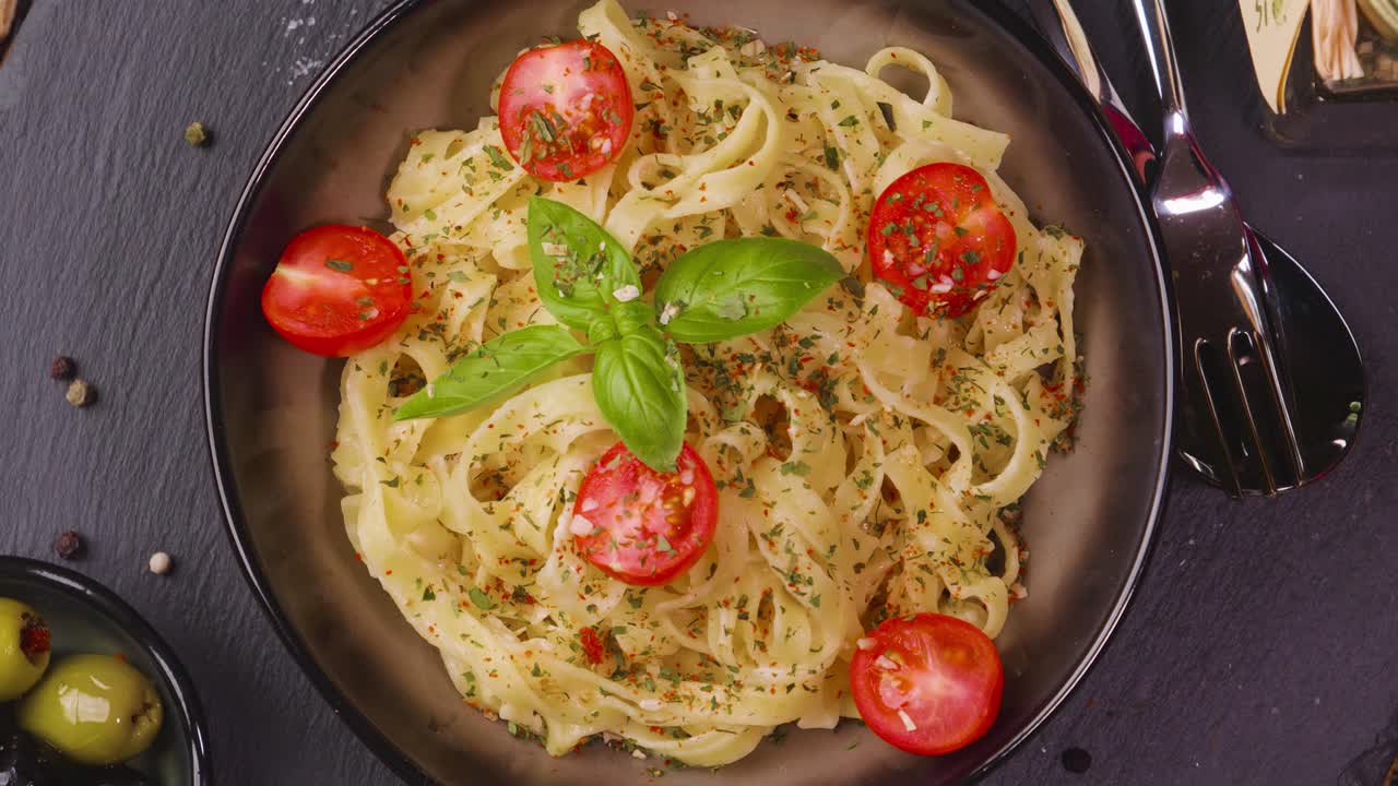 조미료와 토마토를 곁들인 갓 준비한 파스타의 천천히 회전하는 그릇, 슬레이트 접시와 올리브 한 쪽에 제공되는 바질 잎 장식의 조감도