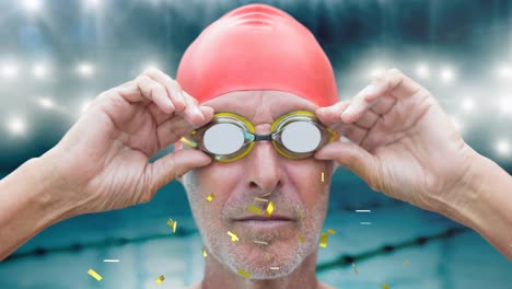 Golden-confetti-falling-over-senior-male-swimmer-wearing-swimming-glasses-against-swimming-pool