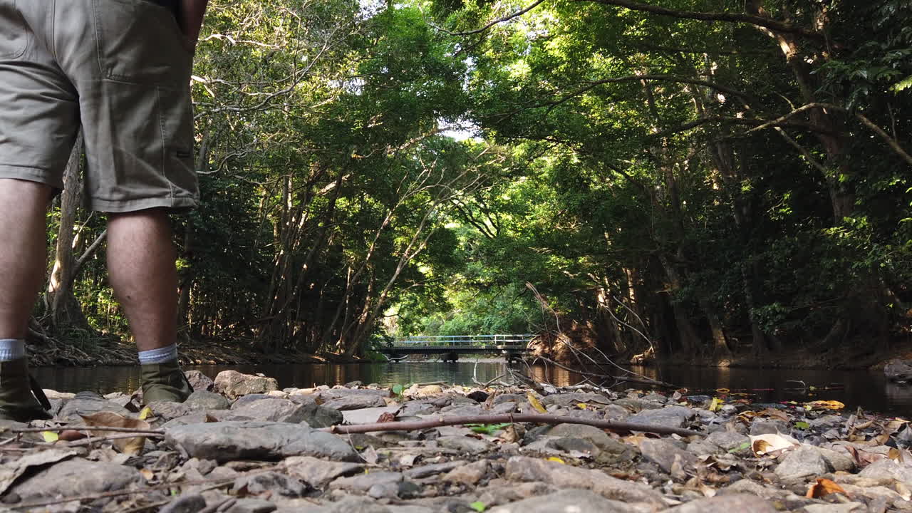 man walking past camera to take in the view of a creek looking downstream