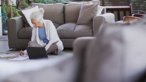 Senior-mixed-race-woman-sitting-on-floor-using-laptop