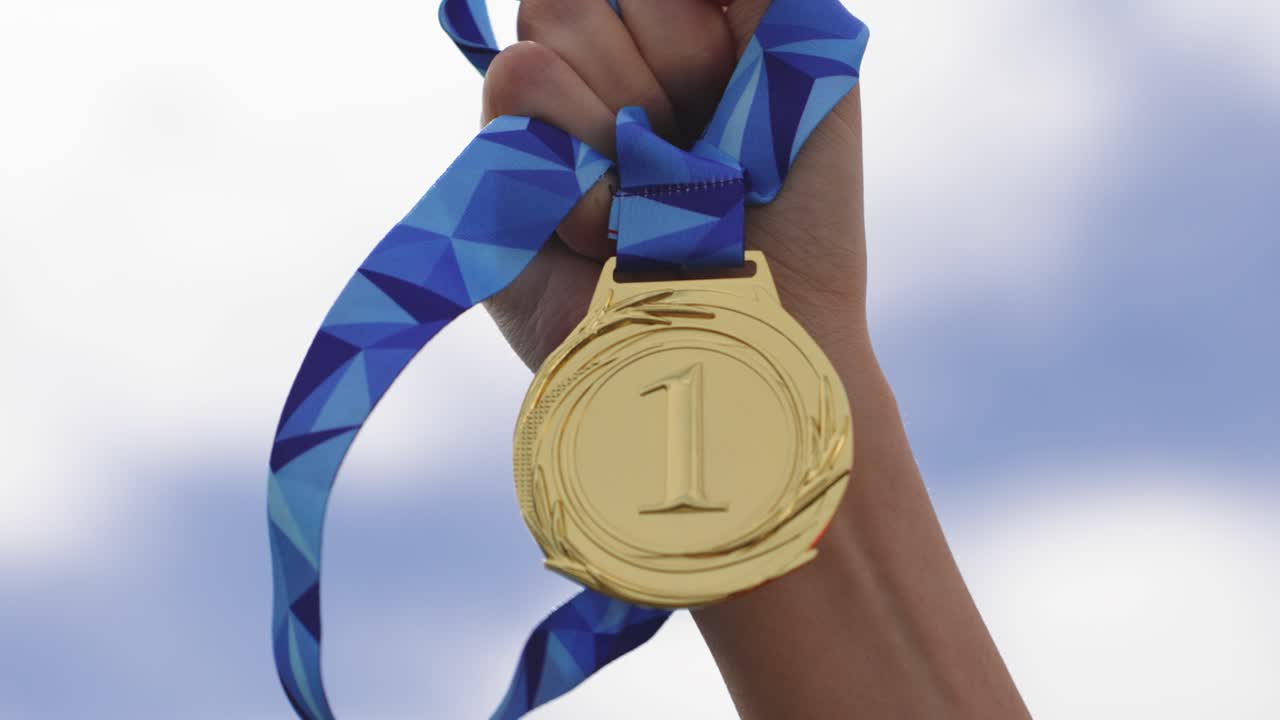 Close-up of a hand holding a winning medal against the sky background. Concept of achievement, success, victory, motivation, reward, and recognition in competition or personal goals