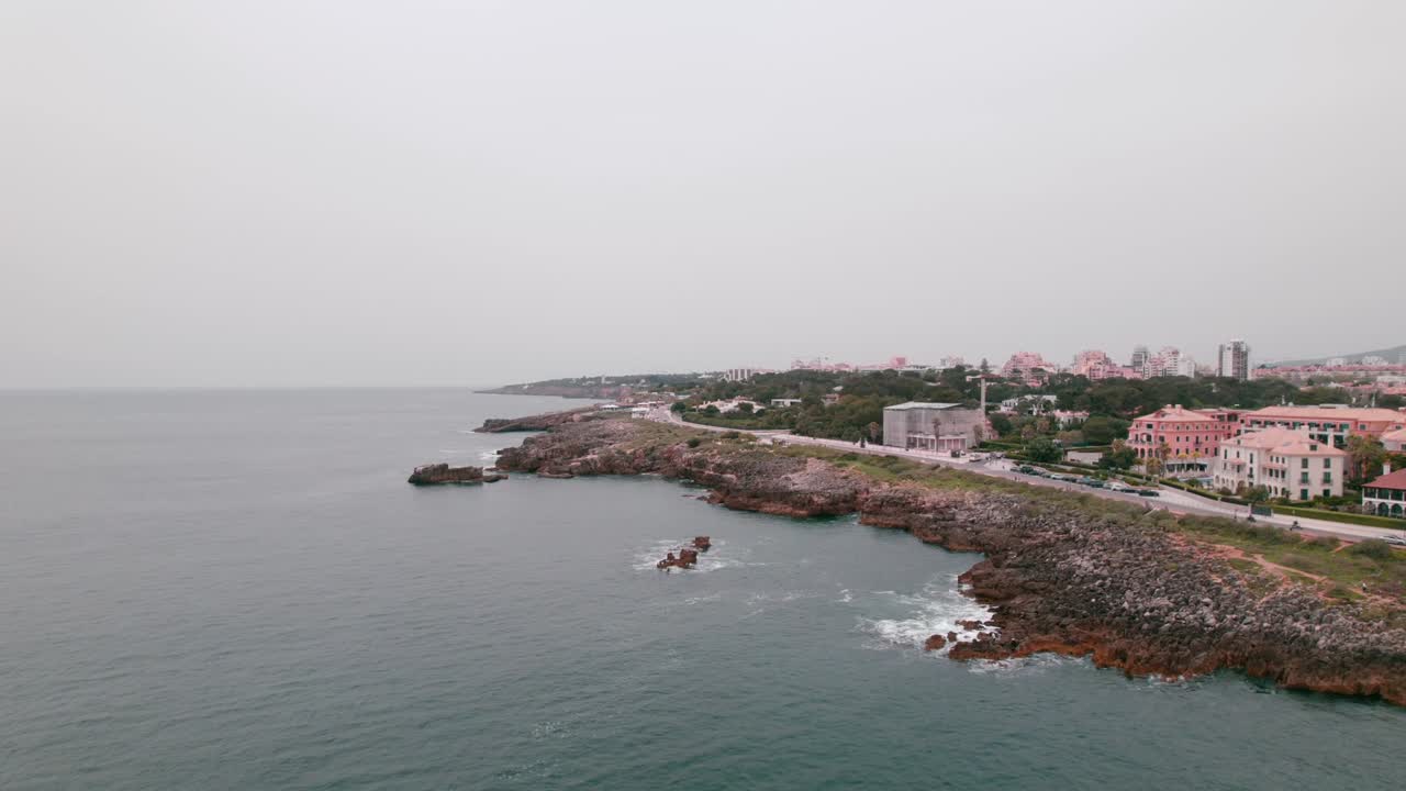 Rugged volcanic coast of Madeira meets still ocean waters, with hillside homes overlooking the shore, blending natural beauty and calm island lifestyle under overcast sky
