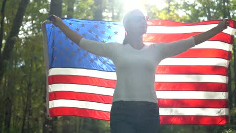 closeup of backlit, pretty blonde woman walking through a forest holding a flag up in the air behind her