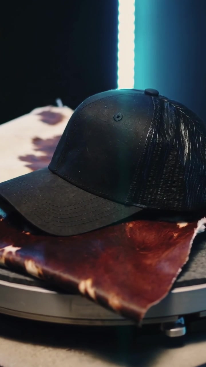 Video verticale: Espositore rotante che rivela un cappellino nero su pelle di mucca con LED blu, per ripresa prodotto.