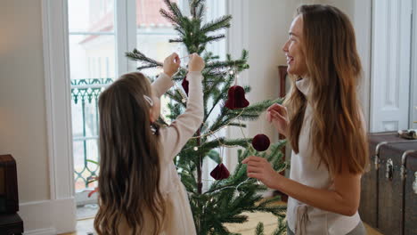 smiling woman decorating christmas tree with girl home. mother helping daughter