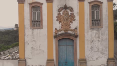 bright blue door with yellow and white facade of our lady of mercy and charity church in ouro preto, minas gerais, brazil, revealing the cemetery next to it and saint fransisco de paulo church behind
