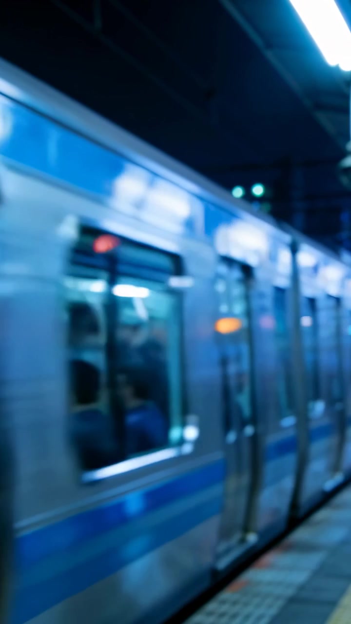 Video verticale: Telecamera che panoramica seguendo un treno lungo la piattaforma, filmando i passeggeri attraverso i finestrini.