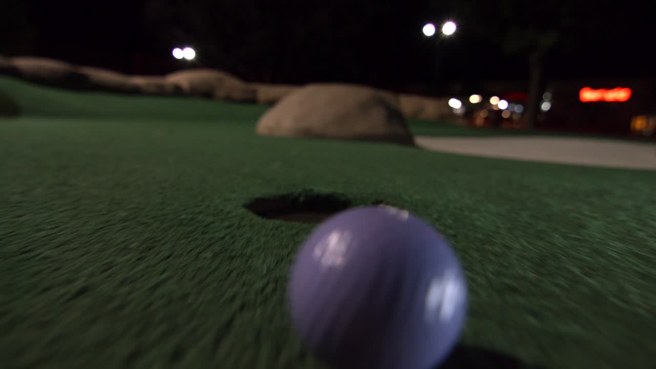 Una pallina da minigolf viola cade nella buca e rimbalza nel raccoglitore su un campo da gioco.