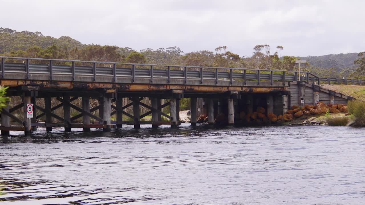 Un rustico ponte di legno si estende su un fiume calmo, circondato da una vegetazione lussureggiante. Ideale per annunci di viaggio, documentari e inquadrature di apertura.
